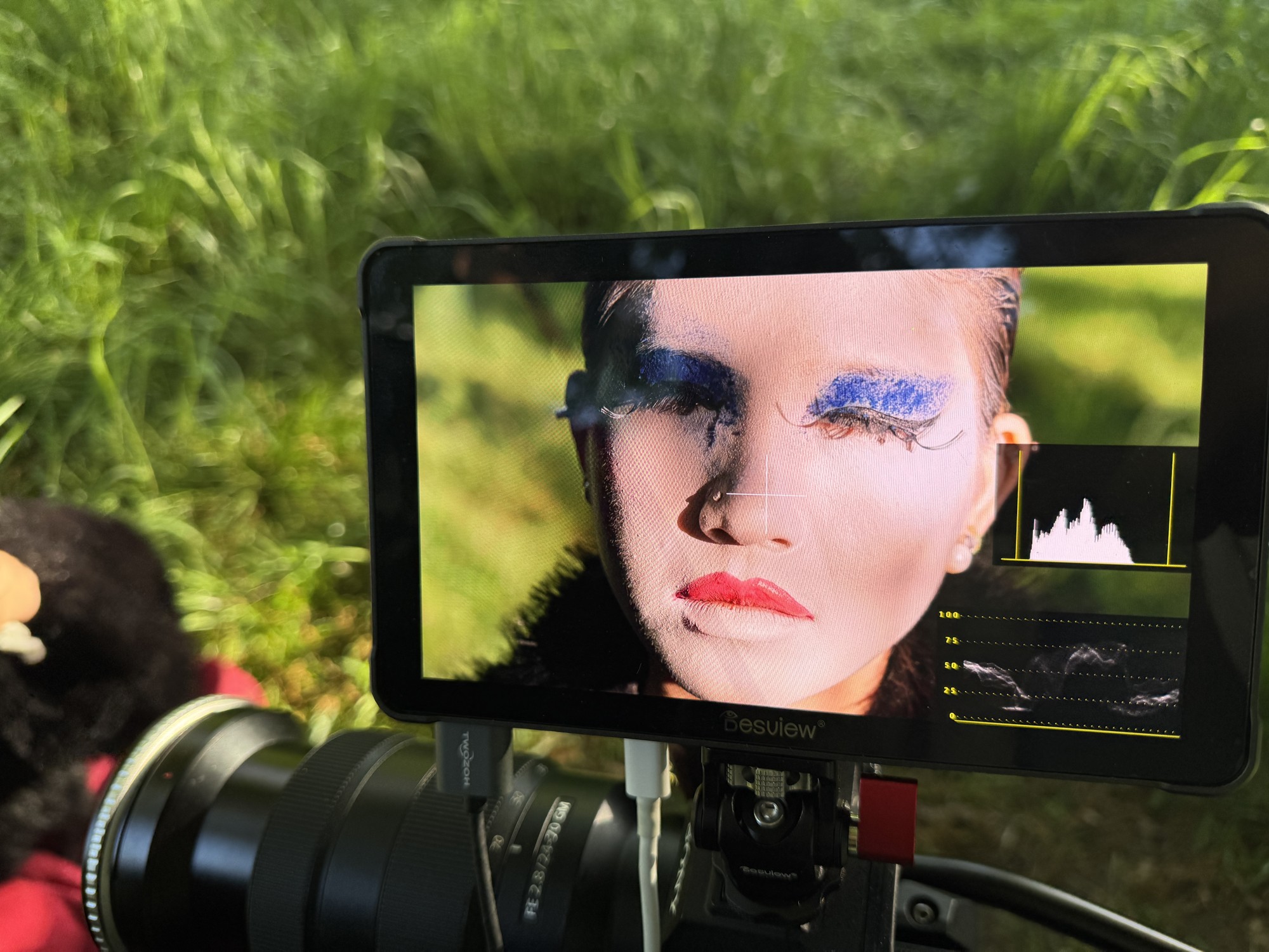 A camera monitor on location displays a close view of blue eye makeup and red lipstick.