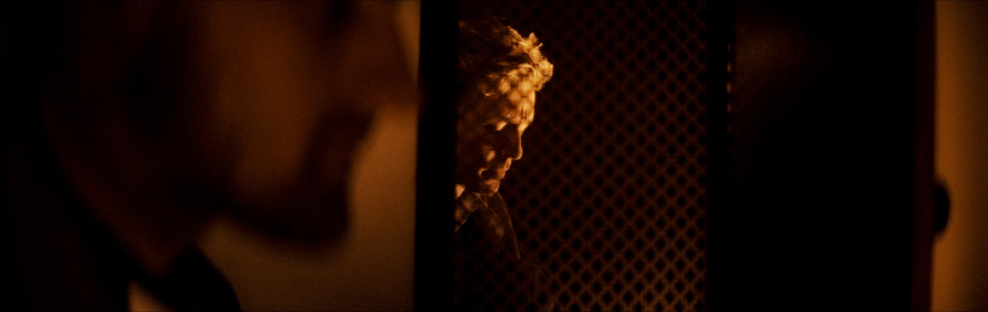 Paul and a priest separated by the dark wooden partition of a confessional.